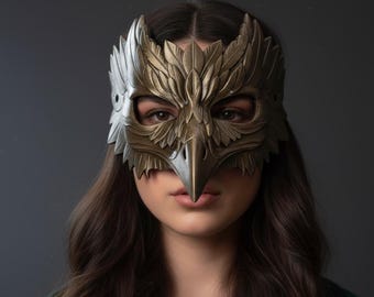 May include: A detailed, metallic bird mask with a prominent beak and feather detailing. The mask is primarily gold and silver, covering the eyes and forehead. The mask is worn by a person with long, dark hair.