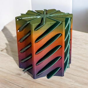 May include: A 3D printed, multi-coloured, geometric object with a gradient of green, orange, and purple. The object has a starburst design on the top and a series of interlocking rings around the sides.