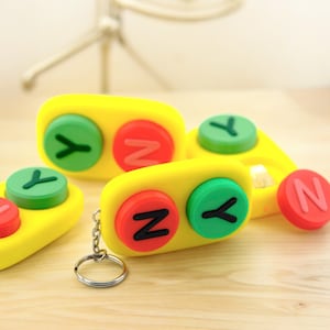 May include: A yellow keychain with three round buttons. Each button has a different letter, Y, Z, and N, in black on a coloured background. The buttons are green, red, and pink.