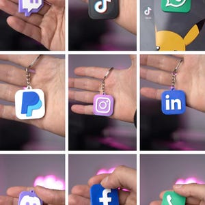 Könnte beinhalten: Eine Sammlung von Schlüsselanhängern mit Logos von Social-Media- und App-Symbolen, darunter Twitch, TikTok, WhatsApp, PayPal, Instagram, LinkedIn, Discord, Facebook und ein Telefonsymbol. Jeder Schlüsselanhänger hat eine andere Farbe und einen silbernen Schlüsselring.