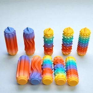 May include: A selection of brightly coloured, cylindrical objects with textured surfaces. The objects have various designs, including wavy and spiky patterns, and are painted in gradients of orange, yellow, blue, and purple.