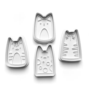 May include: Four white plastic cookie cutters shaped like cats. Each cutter has a different design, including stripes, polka dots, and simple facial features.