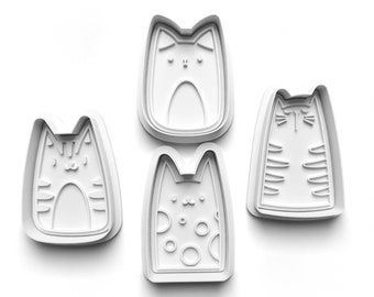 Puede incluir: Cuatro cortadores de galletas de plástico blanco con forma de gato. Cada cortador tiene un diseño diferente, que incluye rayas, lunares y rasgos faciales simples.