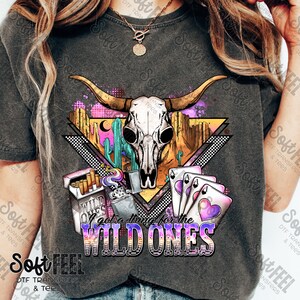 May include: A gray t-shirt with a graphic design featuring a skull, cacti, playing cards, a lighter, and cigarettes. The text "I got a thing for the WILD ONES" is printed on the shirt.