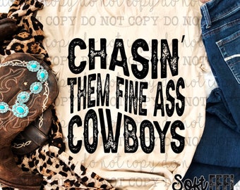 Op de afbeelding: Een beige T-shirt met zwarte tekst die "CHASIN' THEM FINE ASS COWBOYS" luidt. Het shirt ligt op een luipaardprintstof met een bruine leren laars en een turquoise kralenketting.