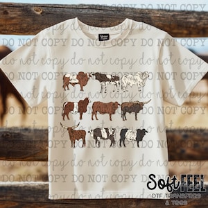 May include: Cream-colored t-shirt featuring a collection of illustrated cattle in various breeds and colors. The design includes brown, black, and white cows. The shirt has the text "Soft Feel" and "DTF Transfers & Tees".
