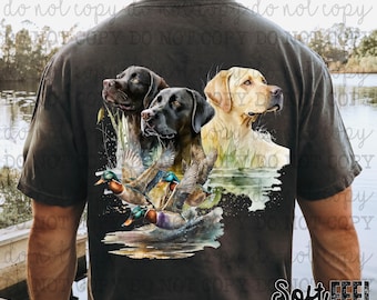 May include: A black t-shirt with a watercolor design of three dogs and ducks. The dogs are a black labrador, a brown labrador, and a yellow labrador. The ducks are flying in the air and swimming in the water. The design is surrounded by green foliage.