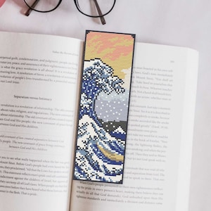 May include: A blue and white bookmark with a pixelated image of a large wave crashing against a mountain. The bookmark is on top of an open book with text about grace and intimacy.