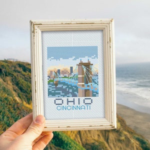 Könnte beinhalten: Ein weiß gerahmter Kreuzstich mit einem blauen und weißen Bild der Skyline von Cincinnati und dem Text "OHIO CINCINNATI".