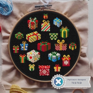 May include: A black and white cross stitch pattern of a variety of colourful gift boxes on a black background. The pattern is framed in a wooden hoop and is labelled "Pattern Keeper TESTED".