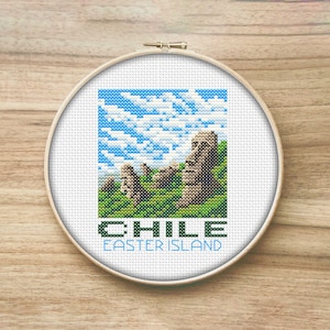 May include: Cross-stitch pattern of the Moai statues on Easter Island, Chile. The pattern is framed in a white hoop with a blue sky and green grass background. The text "CHILE EASTER ISLAND" is below the image.
