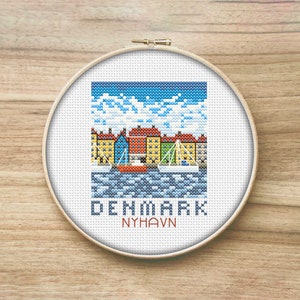 May include: Cross-stitch pattern of a colorful cityscape with boats in a harbor. The text "DENMARK NYHAVN" is below the image.