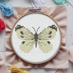 Könnte beinhalten: Ein Kreuzstich-Stickrahmen mit einem gelben Schmetterlingsmotiv. Der Schmetterling hat schwarze Markierungen auf seinen Flügeln.