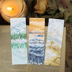 May include: Three colorful bookmarks with different nature scenes. The bookmarks are made of fabric and feature a mountain range with trees, a sunset over the ocean, and a snowy mountain scene.