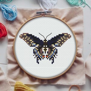 May include: A cross-stitch embroidery hoop featuring a colourful butterfly design. The butterfly is black, blue, yellow and orange. The hoop is made of wood and has a white fabric background.