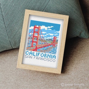 Puede incluir: Patrón de punto de cruz del Puente Golden Gate en San Francisco, California. El patrón presenta un puente rojo con un cielo azul y nubes blancas. El texto "CALIFORNIA SAN FRANCISCO" está debajo del puente.
