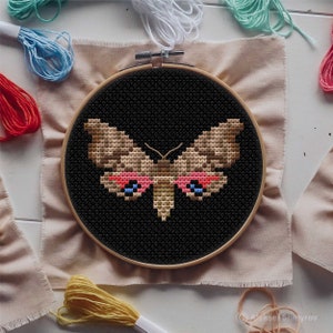 May include: A brown and gold butterfly with pink and blue accents is embroidered on black fabric in a circular embroidery hoop.