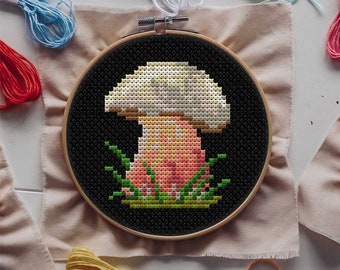 May include: A cross-stitch embroidery hoop with a black background and a colorful mushroom design. The mushroom has a white cap, a pink stem, and green leaves around the base.