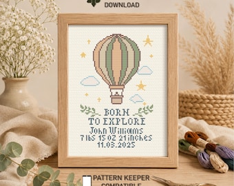 May include: A framed cross-stitch pattern featuring a hot air balloon, stars, and clouds. Text reads: BORN TO EXPLORE, John Williams, 7 lbs 15 oz, 21 inches, 11.03.2025. Includes icons for instant PDF download and pattern keeper compatibility.