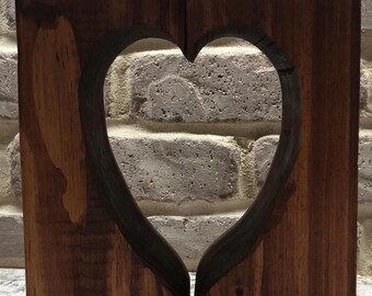 May include: A wooden candle holder shaped like a heart with two white candles. The holder is made of dark brown wood with a natural wood grain.