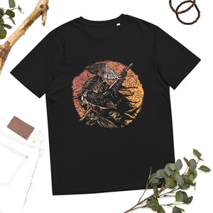 Könnte beinhalten: Schwarzes T-Shirt mit einer detaillierten Illustration eines Samurai-Kriegers mit Schwert und traditionellem Hut, vor einem kreisförmigen Hintergrund in Sonnenuntergangsfarben. Das Design ist in Braun- und Orangetönen gehalten.