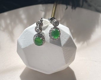 May include: A pair of silver earrings with green gemstone drops surrounded by a halo of smaller clear stones.