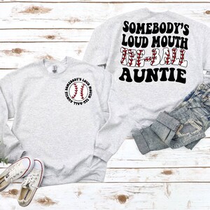 May include: Gray sweatshirt with a baseball graphic and the text "Somebody's Loud Mouth Tee-Ball Auntie" on the front. The back of the sweatshirt has the text "Somebody's Loud Mouth Tee-Ball Auntie" in a retro font.