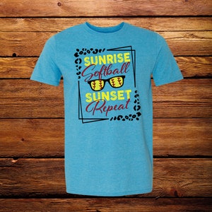 May include: A turquoise blue t-shirt with a black and white graphic print that says "Sunrise Softball Sunset Repeat" with a pair of sunglasses with a softball in each lens.