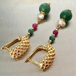 Peut inclure: Une paire de boucles d'oreilles pendantes en or avec une base en anneau doré texturé et ajouré. Chaque boucle est ornée d'une tige verticale de perles, incluant une grosse sphère verte, une perle blanche, une petite perle rose et une petite verte.