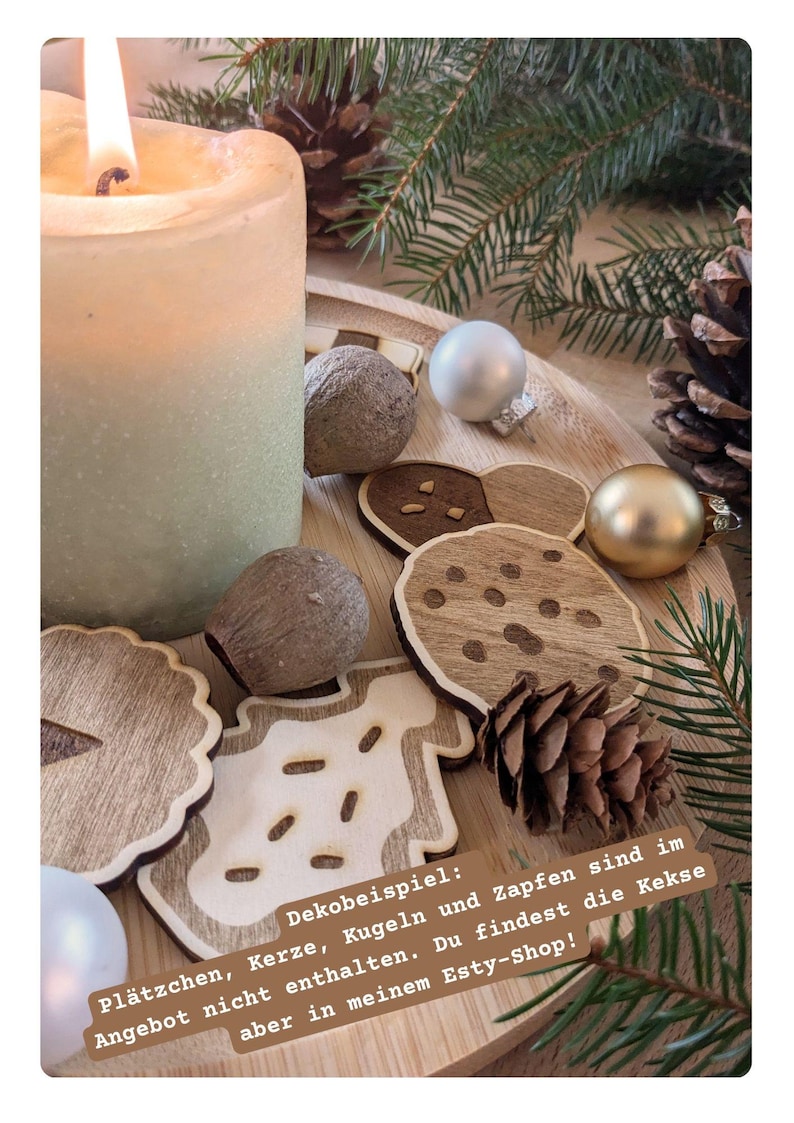 May include: A lit candle next to wooden Christmas ornaments, pine cones, and greenery on a wooden tray. The image includes wooden cookie-shaped decorations and text in German.