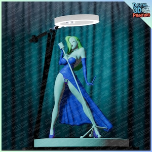 Op de afbeelding: 3D-geprinte figuur van een zangeres in een blauwe jurk, met een microfoon. De figuur heeft groen haar en staat op een podium met een schijnwerper. De achtergrond is een herhaald patroon van tekst.