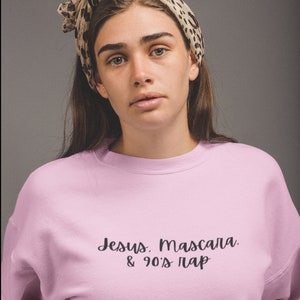 Pode incluir: Uma camisa de moletom rosa com o texto "Jesus. Mascara. & 90's Pap" em letras cursivas pretas.