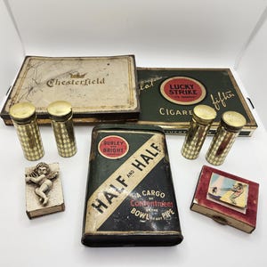 May include: An assortment of vintage tobacco-related items, including Chesterfield and Lucky Strike cigarette boxes, metal cigarette cases with diamond patterns, and a Half and Half tobacco tin. Also, a small box with a cherub and a small box with a surfer.