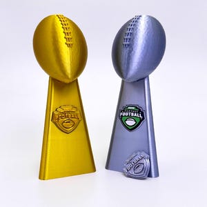 May include: Two football-shaped trophies. One is gold, the other is silver. Both have a football at the top and a trapezoid base. The gold trophy has the word "FOOTBALL" on the base. The silver trophy has the words "ESPN FANTASY FOOTBALL".