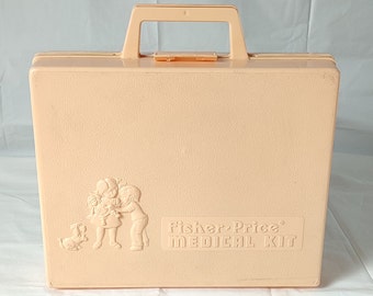 May include: A light pink plastic toy medical kit with a handle. The front of the case has a raised image of a doctor, a nurse, and a child. The text "Fisher-Price® MEDICAL KIT" is printed on the front of the case.