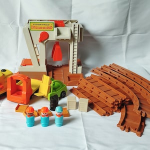 May include: A vintage Fisher-Price Lift & Load Railroad toy set with a crane, train, cars, track pieces, and three construction worker figures. The set is made of plastic and is in good condition.
