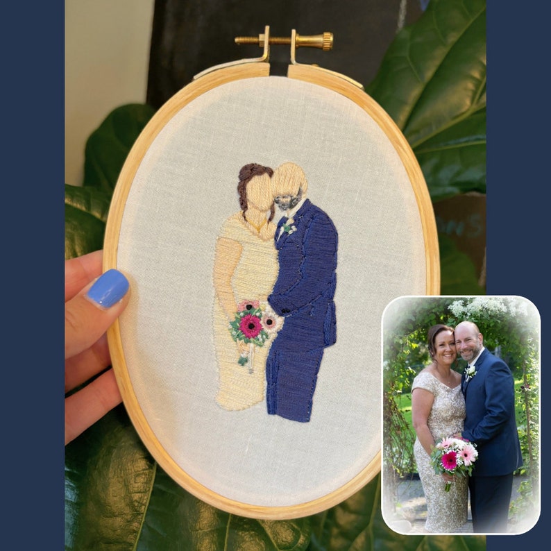 Op de afbeelding: Borduurwerk in een ronde hoepel met daarop een stel in trouwtenue. De bruid draagt een witte jurk en de bruidegom een blauw pak. Ze houden een boeket met roze en rode bloemen vast.