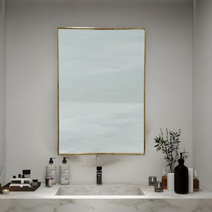 May include: A white bathroom vanity with a marble countertop and a gold framed mirror. The vanity has two drawers and a shelf. There are towels and toiletries on the countertop.