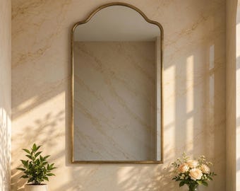 Puede incluir: Un espejo de pared arqueado con un marco dorado fino cuelga sobre una encimera de mármol verde oscuro. El tocador cuenta con un grifo dorado, una pila de toallas blancas dobladas, una pequeña planta verde y un jarrón de cristal con rosas color melocotón.