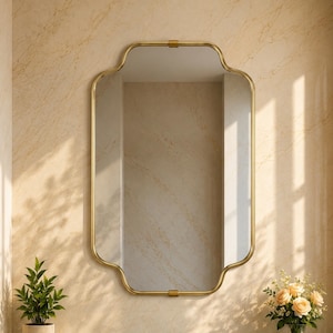 Pode incluir: Um espelho de parede retangular com cantos arredondados e uma moldura de metal dourado. O espelho apresenta um design distinto de bordas recortadas ao longo das laterais e do topo, oferecendo uma superfície reflexiva sobre uma bancada de mármore verde.