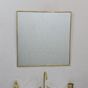 May include: A white porcelain bathroom sink with a gold faucet and a gold framed mirror above it. There is a gold soap dispenser and a gold cup on the counter.