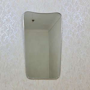 May include: A silver-framed, wavy-edged mirror hangs on a wall with a white and silver patterned wallpaper.
