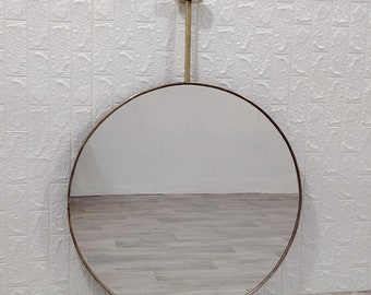 May include: A round, gold-framed mirror with a hanging strap. The mirror is reflecting a white tiled wall and a wooden floor.