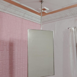 Pode incluir: Um espelho com moldura prateada pendurado no teto em uma sala com paredes de tijolo rosa e molduras brancas.