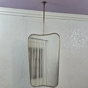 May include: A vintage-style, rectangular mirror with a curved top edge, suspended from the ceiling by a metal rod. The mirror has a thin, gold-colored frame and a clear, plastic shower curtain is visible behind it.