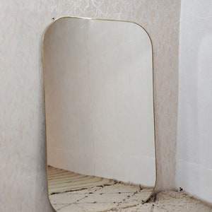 May include: A large, rectangular mirror with a gold-colored frame. The mirror has rounded edges and is leaning against a wall.