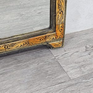 May include: A large, rectangular mirror with a decorative frame. The frame is made of wood and is inlaid with bone or ivory. The frame is decorated with intricate floral patterns. The mirror is in good condition and has a slight patina.