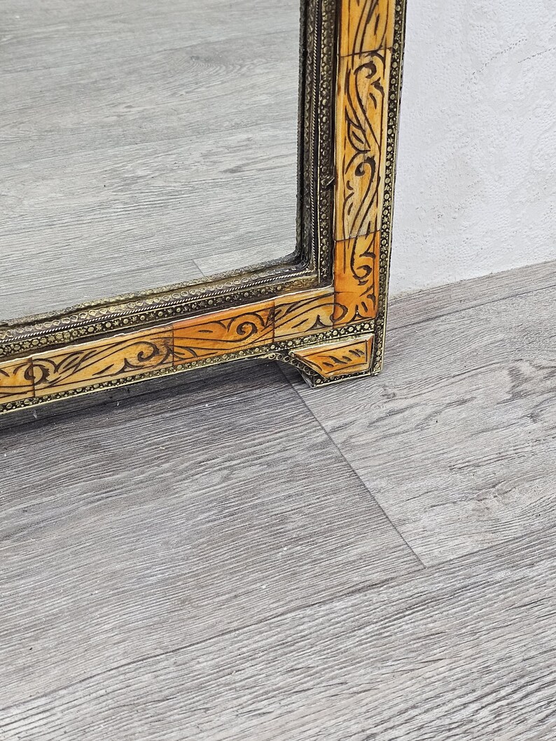 May include: A large, rectangular mirror with a decorative frame. The frame is made of wood and is inlaid with bone or ivory. The frame is decorated with intricate floral patterns. The mirror is in good condition and has a slight patina.