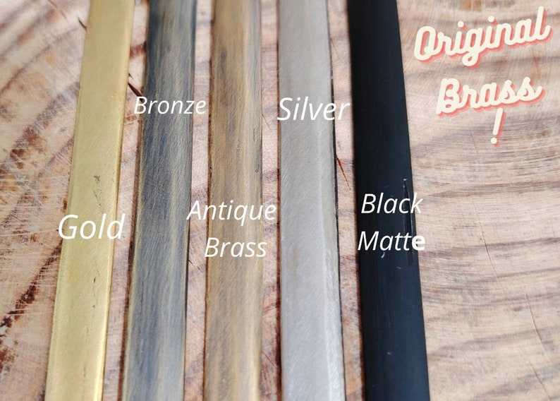 May include: Close-up of five metal strips in different finishes: gold, bronze, antique brass, silver, and black matte. The text "Original Brass!" is written in red on the right side of the image.