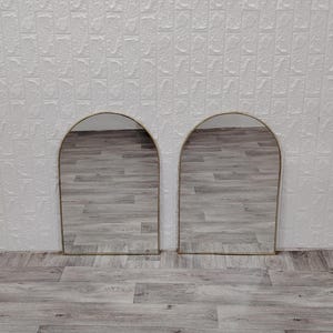 Op de afbeelding: Twee gouden boogspiegels met een houten vloer erachter.